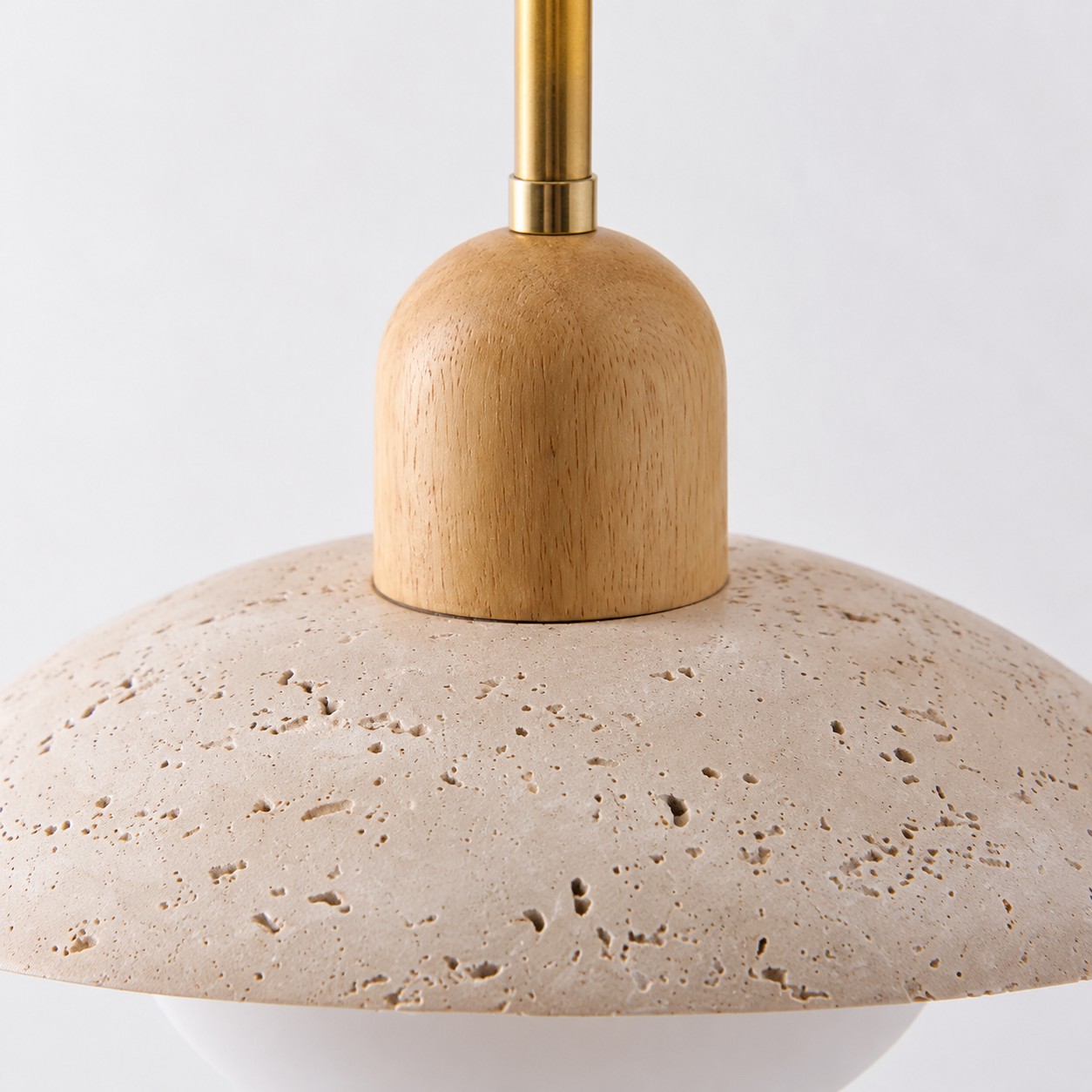 Brass arm meeting a light wood collar on the travertine disc