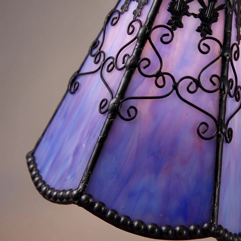 Primer plano de una pantalla de vidrieras Tiffany de color azul violáceo con detalles en volutas negras y borde perlado.