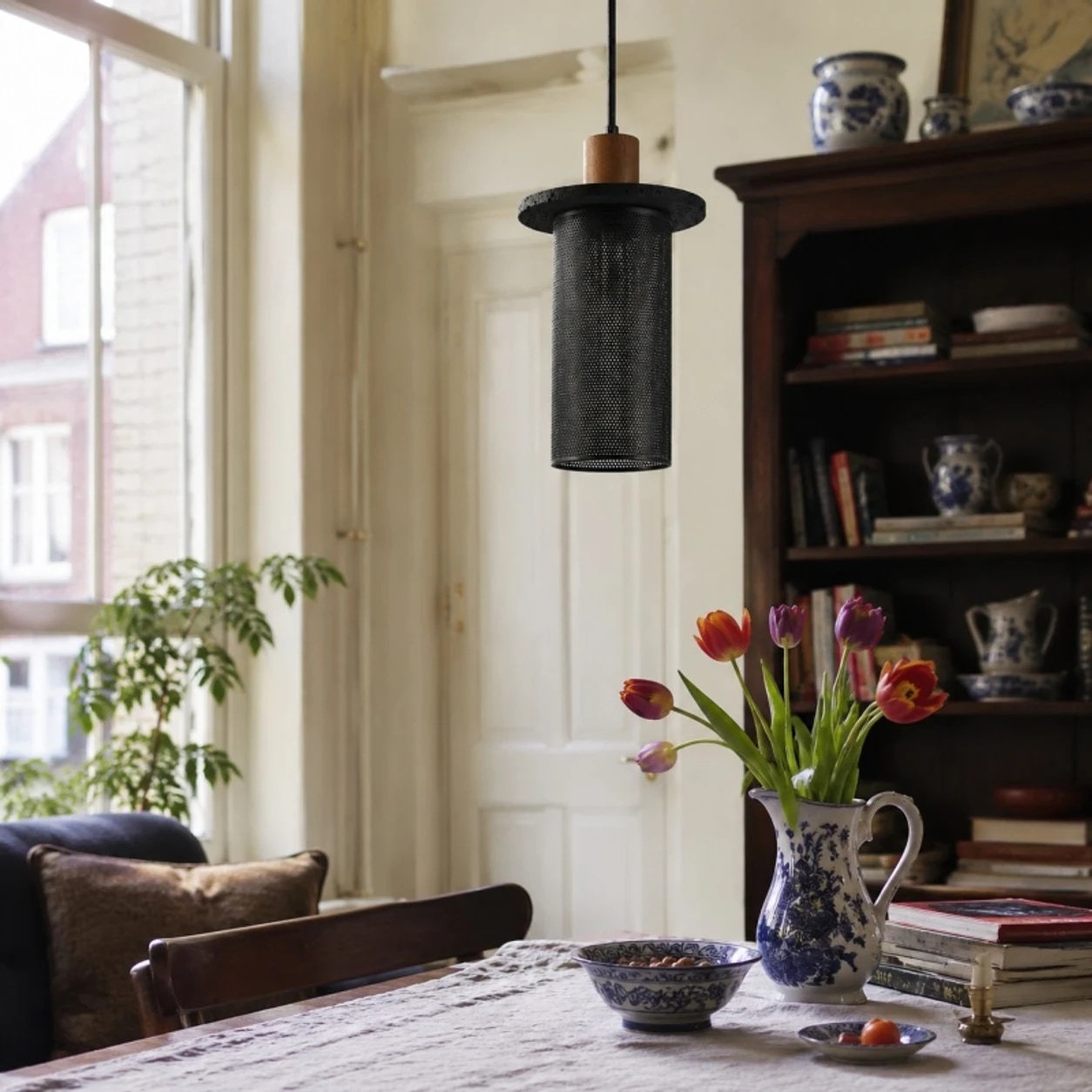 Lámpara colgante de malla tejida negra sobre una mesa de comedor junto a la ventana.