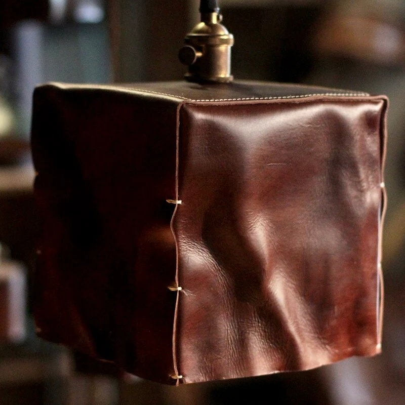 Detailweergave van een bruine, handvormige leren hanglamp met lampenkap.