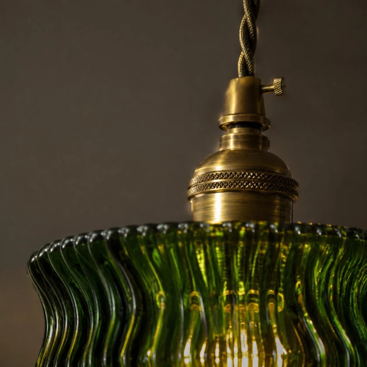Mässingsfärgad lamphuvuddetalj ovanför den gröna glasskärmen