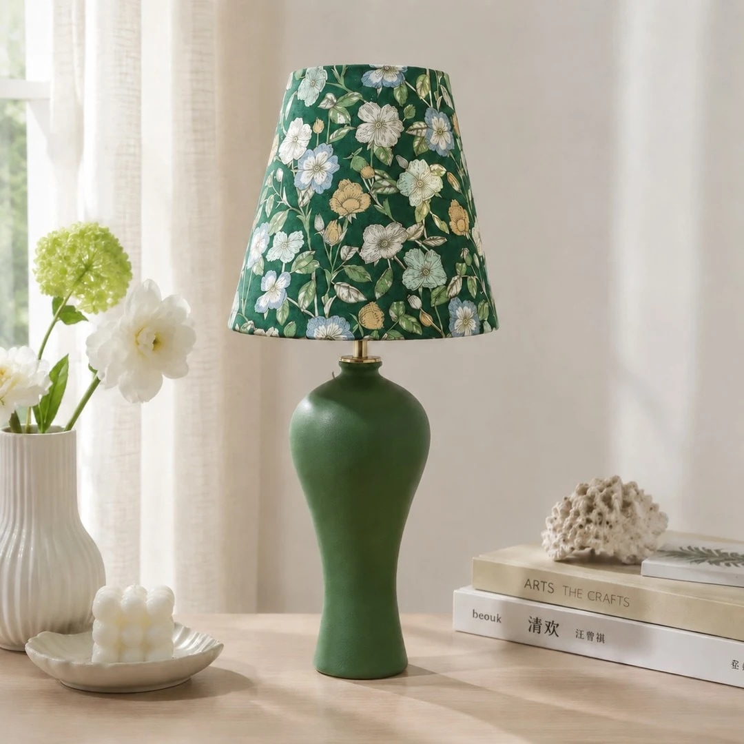 Lampe de table en céramique verte à motif floral, placée près d'une fenêtre lumineuse.