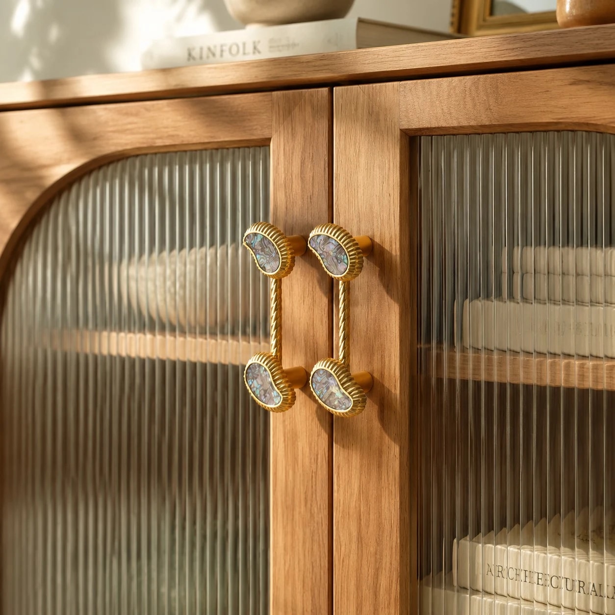 Shell brass cabinet pulls on warm wood and fluted glass doors
