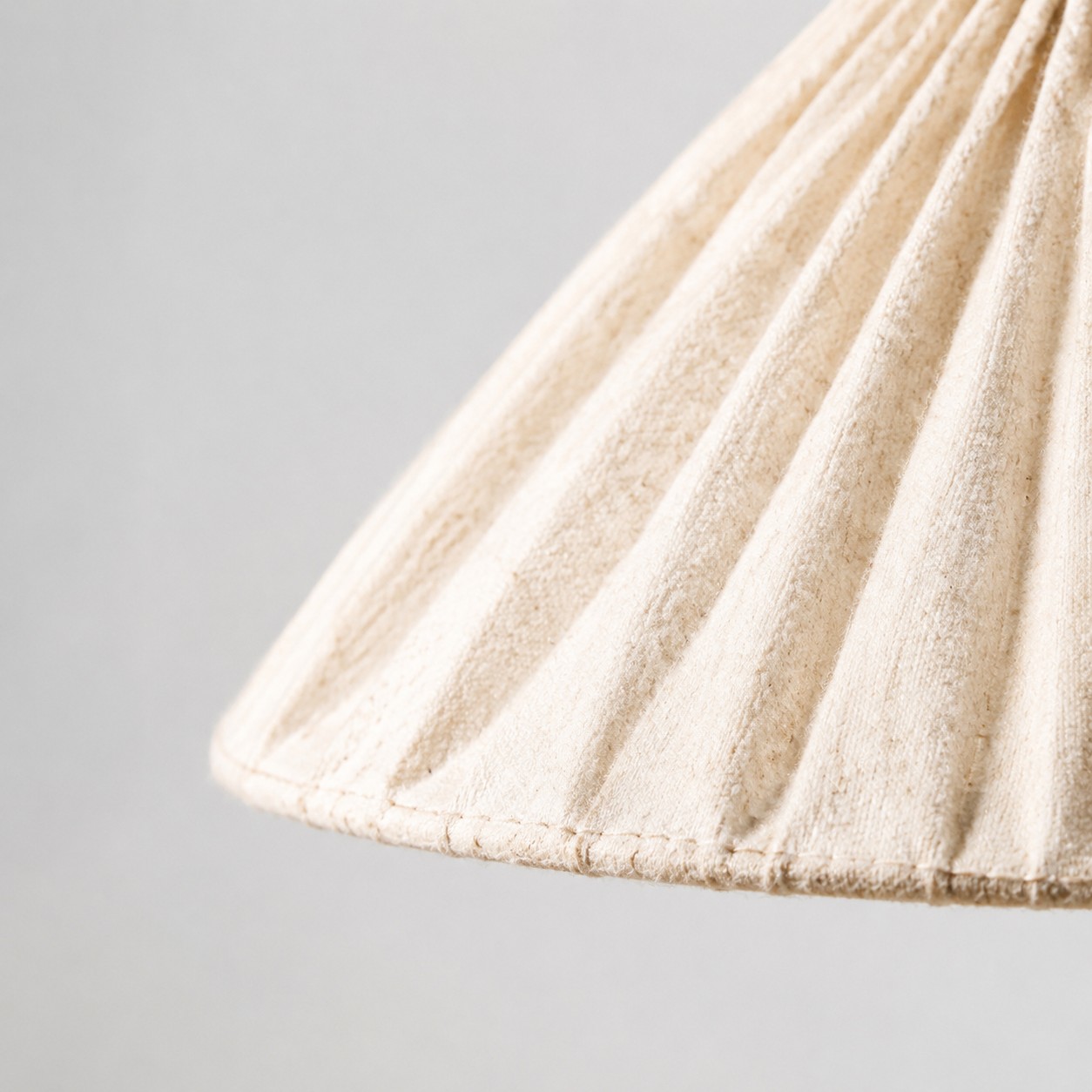 Gros plan sur le tissage en lin naturel, les plis cousus et le bord fini de l’abat-jour