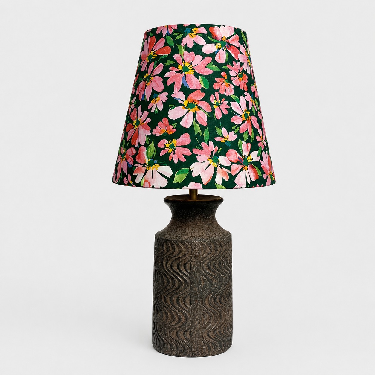 Vista frontal de una lámpara de mesa con pantalla de tela floral y base de cerámica oscura texturizada