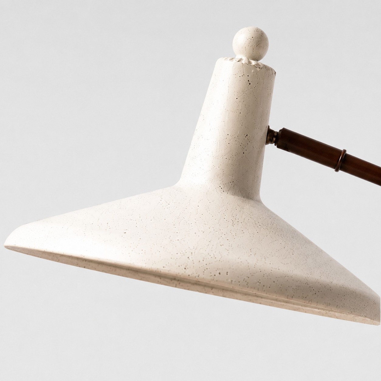 Detailopname van een lampenkap van getextureerd ivoorkleurig metaal en een afgeronde sierknop.