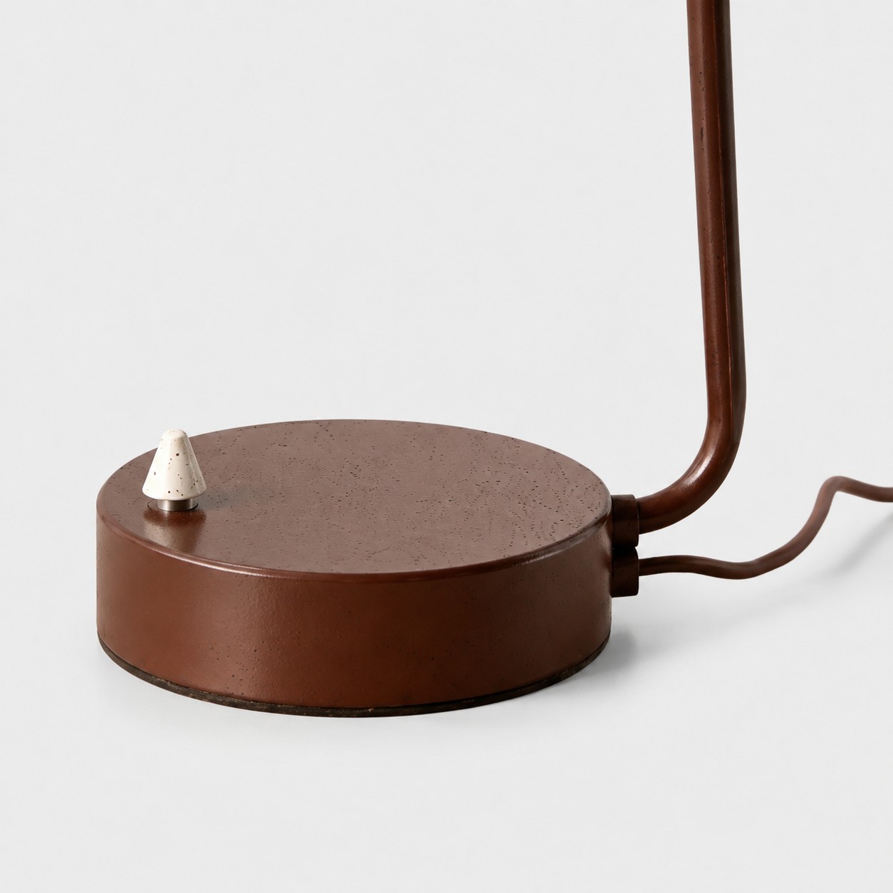 Detailopname van een bruine ronde lampvoet en een metalen aan/uit-schakelaar.