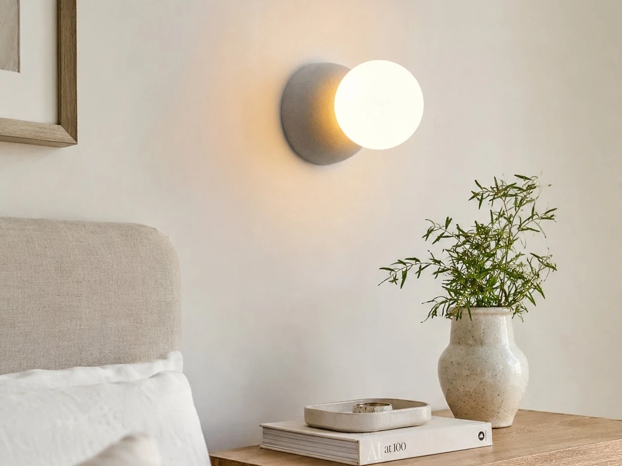 Grey concrete and opal glass wall light installed beside a bed