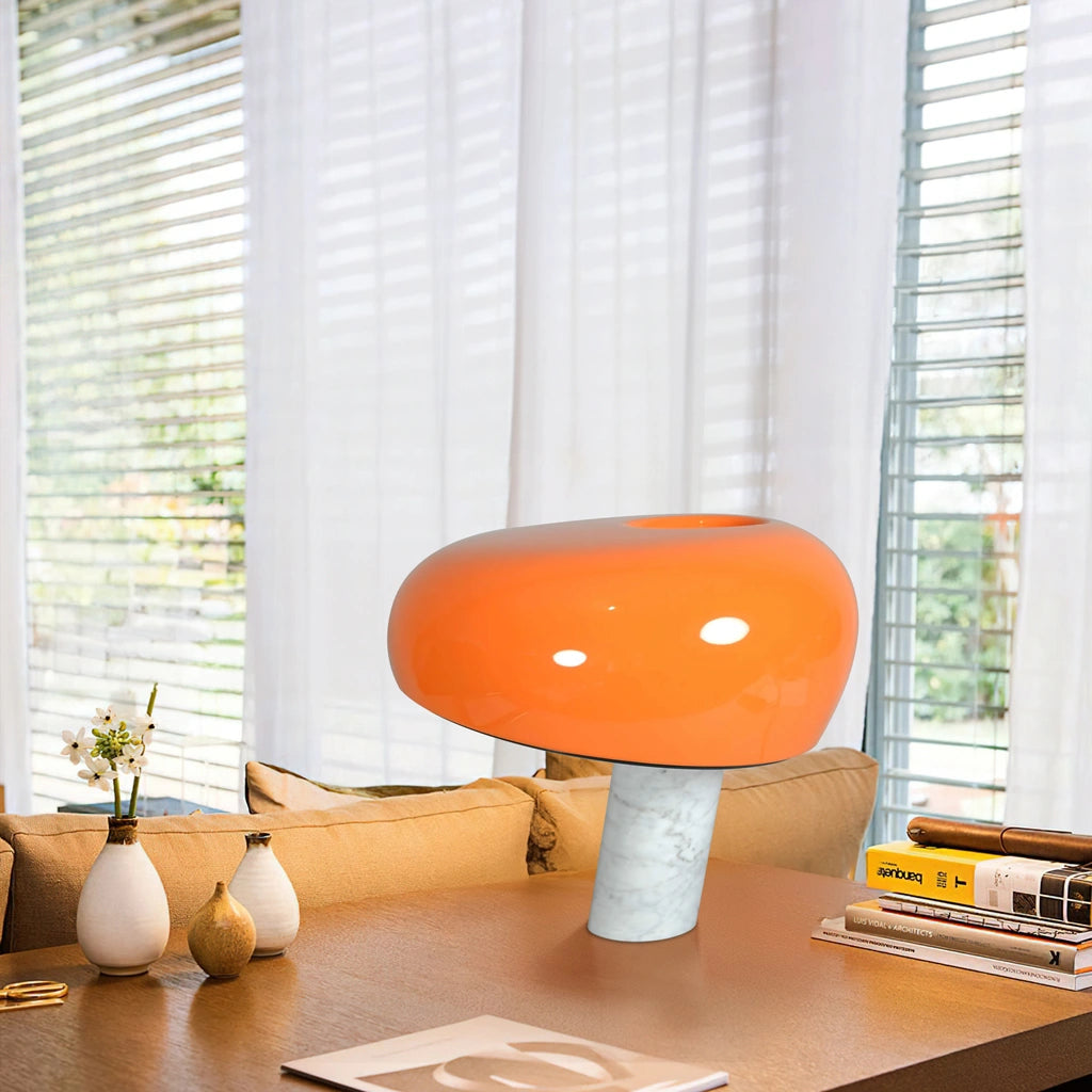 Eine orange Pilzlampe steht auf einem Holzschreibtisch an einem hellen Fenster.