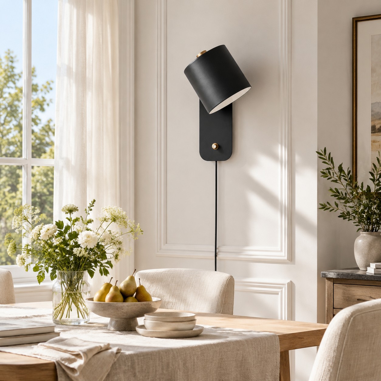 Lampada da parete cilindrica nera sopra un tavolo da pranzo, illuminata dalla luce del giorno.